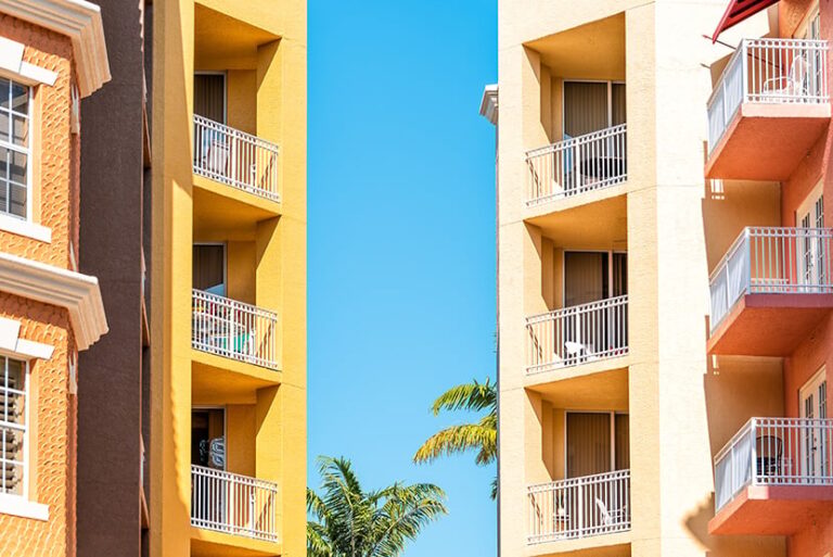 Colorful condos, condominiums colorful, orange yellow multicolored buildings facade exterior with windows, palm trees, mansion real estate property in Florida or Spain
